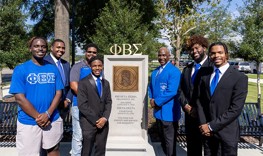 Phi Beta Sigma members and alumni stand in front of their sign at the NPHC plaza